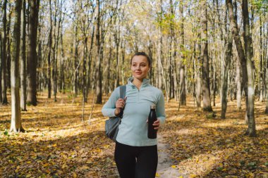 Kız demir şişeden su içiyor, plastikten değil. Güzel bir kız güneşli bir sonbahar ormanında dışarıda spor yapıyor. Vücut pozitifliği, kadınlar için spor, sağlıklı yaşam tarzı, kendini sevme ve sağIık.