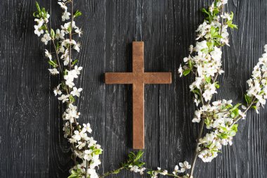 Ahşap bir arka planda İsa 'nın dirilişi yazılı çiçeklerle çapraz yap. Paskalya konsepti. İsa Mesih 'in ölümünü ve dirilişini simgeliyor.