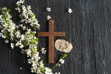 Ahşap bir arka planda İsa 'nın dirilişi yazılı çiçeklerle çapraz yap. Paskalya konsepti. İsa Mesih 'in ölümünü ve dirilişini simgeliyor.