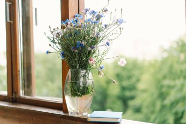 Pencere kenarında güzel bir yaz, sakin bir hayat. Bir buket çiçek ve rahat bir evin pencere eşiğinde bir kitap..