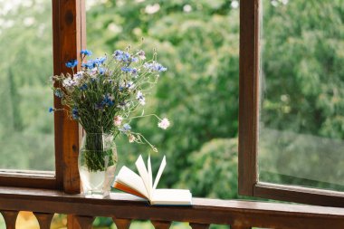 Pencere kenarında güzel bir yaz, sakin bir hayat. Bir buket çiçek ve rahat bir evin pencere eşiğinde bir kitap..
