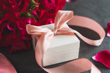 Şenlikli hediye kutusu sürprizi. Üst manzara beyaz hediye kutusu, canlı pembe kurdeleyle süslenmiş, kırmızı güllerle çevrili. Güzel bir tebrik kartı.