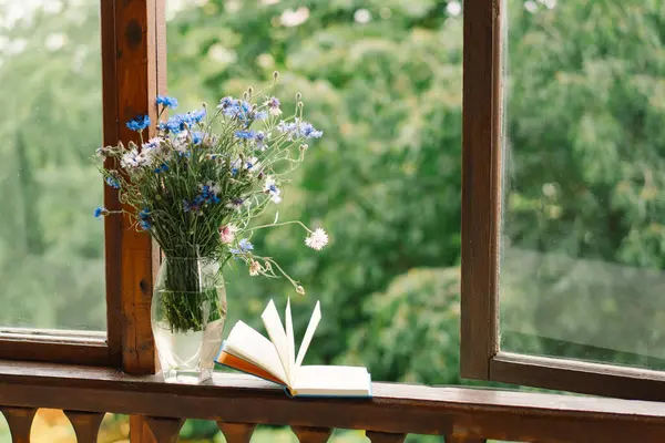 Pencere kenarında güzel bir yaz, sakin bir hayat. Bir buket çiçek ve rahat bir evin pencere eşiğinde bir kitap..