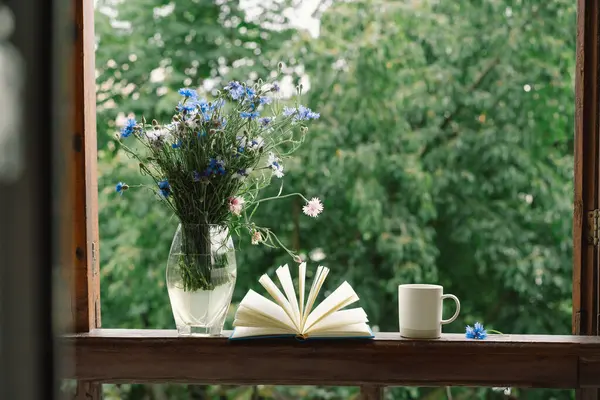 Pencere kenarında güzel bir yaz, sakin bir hayat. Bir buket çiçek ve rahat bir evin pencere eşiğinde bir kitap..