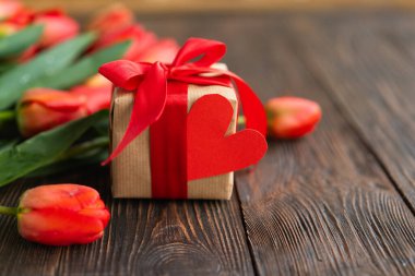 Bir buket taze turuncu laleler hediye kutusu ve ahşap zemin üzerinde kırmızı kağıt kalpler. Sevgililer Günü, Kadınlar Günü ve Anneler Günü için fotokopi alanı olan tebrik kartı..