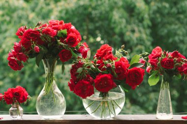 Vazoda bir buket kırmızı gül ve tahta pencere pervazında bir kitap. Eski bir kır evinin penceresinde, yazlık evde hala hayat var. Çiçekli ev dekorasyonu.