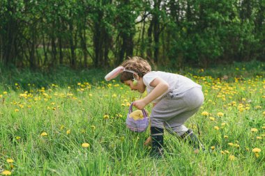 Yumurta sepeti ve tavşan kulaklı komik çocuk güneşli bahar bahçesinde Paskalya yumurtası avında. Paskalya yumurtası avlamak