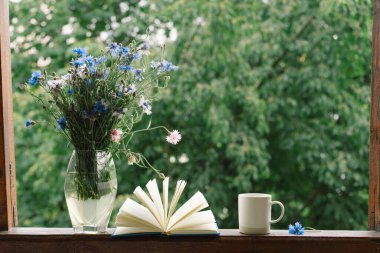 Pencere kenarında güzel bir yaz, sakin bir hayat. Bir buket çiçek ve rahat bir evin pencere eşiğinde bir kitap..