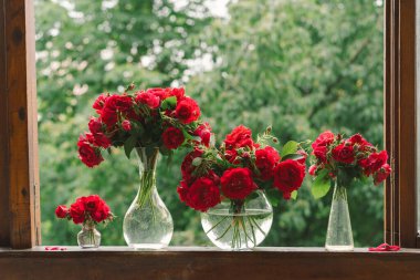 Vazoda bir buket kırmızı gül ve tahta pencere pervazında bir kitap. Eski bir kır evinin penceresinde, yazlık evde hala hayat var. Çiçekli ev dekorasyonu.