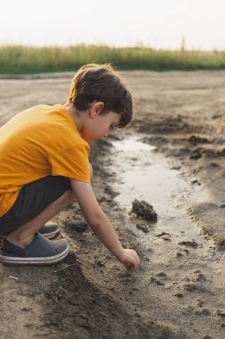 Doğadaki bir çocuğun portresi. Turuncu tişörtlü bir çocuk doğada çamurla oynar. Mutlu çocuk, yaşam tarzı. Gizli Portreler.