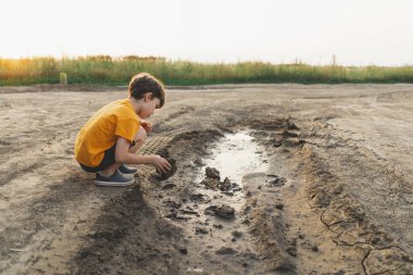 Doğadaki bir çocuğun portresi. Turuncu tişörtlü bir çocuk doğada çamurla oynar. Mutlu çocuk, yaşam tarzı. Gizli Portreler.