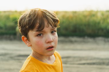 Doğadaki bir çocuğun portresi. Turuncu tişörtlü bir çocuk doğada ağlıyor. Olumsuz çocuk, yaşam tarzı.