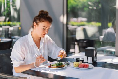 Beyaz gömlekli bir kadın bir kafede öğle yemeği ya da dışarıda kahvaltı yapar. Restoran terasında sağlıklı yemek yiyen bir kadın.