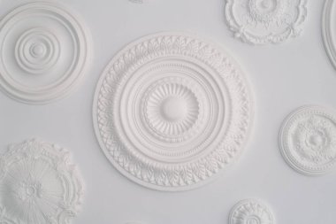 Çeşitli desenlere sahip sanatsal beyaz dairesel kabartma heykellerin bir koleksiyonu el değmemiş beyaz bir arkaplan karşısında düzenlenir, dokulara vurgu yapan minimalist bir estetik sergiler.