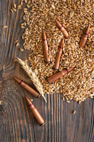 stock image Wheat grains are spread across a wooden table, interspersed with several metal bullet shells. The concept of the photo suggests that grain can be used as a weapon. Hunger as a weapon against humanity