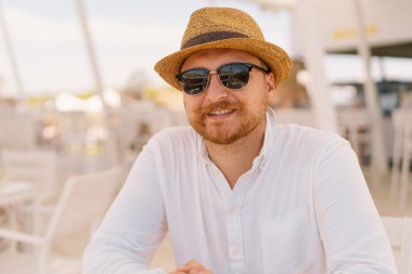 Beyaz gömlekli ve Hasır Şapkalı Gülümseyen Adam Açık Deniz Kafesi 'nde güneş gözlüğü takıyor.