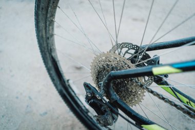 Bu görüntü, dağ bisikletlerinin arka tekerlekleri ve kasetlerinin yakın çekimini gösteriyor. Tekerlek çamurla kaplı ve kaset çok yıpranmış. Görüntü alçaktan çekiliyor, direksiyona bakıyor..