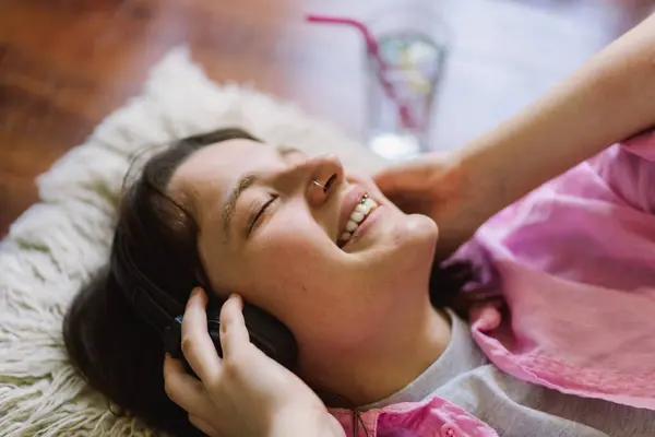 stock image A teengirl is lying on her back on a wooden floor, wearing headphones and a pink shirt. She has her eyes closed and is smiling, seemingly relaxed and listening to music.