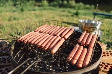 Nehir kenarında güneşli bir günde barbekü. Izgara etle dolu ve yanında bir tuğla tabanında çaydanlık duruyor. Izgaradan duman yükselir, havayı ızgara yiyecek kokusuyla doldurur..