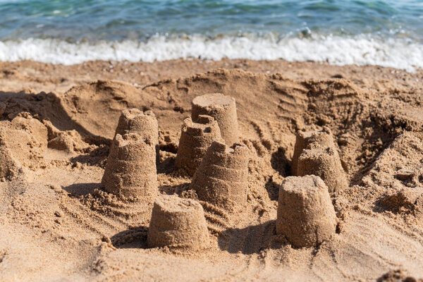 A collection of small sandcastles are built on the sandy beach near the ocean. The tide is out and the waves are rolling in the distance.
