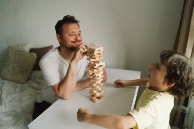 Bir baba ve oğlu kapalı alanda kule oyunu oynuyorlar. Oyun beyaz bir masada geçiyor ve arka plan odak dışı. Babalar Günü