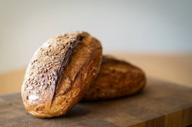 İki somun ekşi ekmek, taze pişmiş ve hala sıcak, ahşap bir yüzeye istiflenmiştir. Somunlar susam ve ayçiçeğiyle kaplıdır. Köy ve lezzet katar..