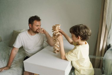 Bir baba ve oğlu kapalı alanda kule oyunu oynuyorlar. Oyun beyaz bir masada geçiyor ve arka plan odak dışı. Babalar Günü