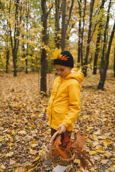 stock image A joyful child dressed in a bright yellow raincoat walks along a serene forest path covered with vibrant autumn leaves. Autumn mood. Beautiful autumn