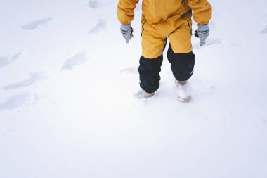 Parlak sarı ceketli neşeli bir çocuk kış boyunca taze karda oynuyor.