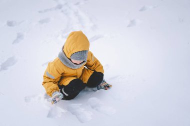 Parlak sarı ceketli neşeli bir çocuk kış boyunca taze karda oynuyor.