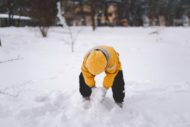 Parlak sarı ceketli neşeli bir çocuk kış boyunca taze karda oynuyor.