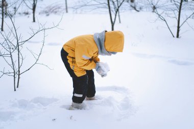 Parlak sarı ceketli neşeli bir çocuk kış boyunca taze karda oynuyor.