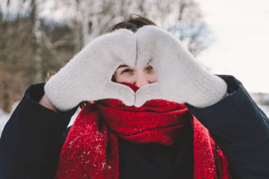 Kırmızı eşarplı gülümseyen bir kadın, parlak mavi gökyüzünün altındaki sakin bir ormanda karlı bir kış gününün tadını çıkarıyor. Noel ve Yeni Yıl Kutlama Konsepti.