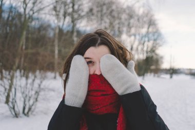 Kırmızı eşarplı gülümseyen bir kadın, parlak mavi gökyüzünün altındaki sakin bir ormanda karlı bir kış gününün tadını çıkarıyor. Noel ve Yeni Yıl Kutlama Konsepti.