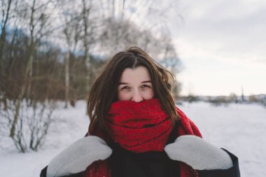 Kırmızı eşarplı gülümseyen bir kadın, parlak mavi gökyüzünün altındaki sakin bir ormanda karlı bir kış gününün tadını çıkarıyor. Noel ve Yeni Yıl Kutlama Konsepti.