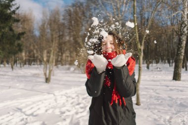 Kırmızı eşarplı gülümseyen bir kadın, parlak mavi gökyüzünün altındaki sakin bir ormanda karlı bir kış gününün tadını çıkarıyor. Noel ve Yeni Yıl Kutlama Konsepti.