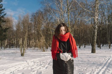 Kırmızı eşarplı gülümseyen bir kadın, parlak mavi gökyüzünün altındaki sakin bir ormanda karlı bir kış gününün tadını çıkarıyor. Noel ve Yeni Yıl Kutlama Konsepti.