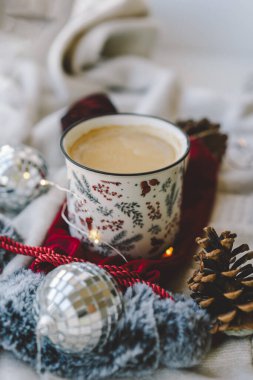Sıcak bir içecek, bir hediye ve bayram süslerinin yanındaki dekoratif bardakta durur. Kış rahatlığı için mükemmel sıcak bir ortam yaratır..