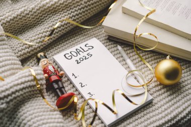 A warm setting featuring a list titled Goals 2025, a cozy knit sweater, festive candy canes, and decorative elements, perfect for New Years planning. clipart