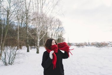 Kırmızı eşarplı gülümseyen bir kadın, parlak mavi gökyüzünün altındaki sakin bir ormanda karlı bir kış gününün tadını çıkarıyor. Noel ve Yeni Yıl Kutlama Konsepti.