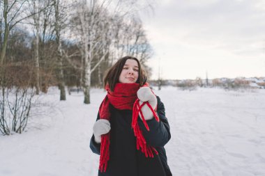 Kırmızı eşarplı gülümseyen bir kadın, parlak mavi gökyüzünün altındaki sakin bir ormanda karlı bir kış gününün tadını çıkarıyor. Noel ve Yeni Yıl Kutlama Konsepti.