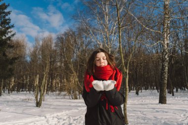 Kırmızı eşarplı gülümseyen bir kadın, parlak mavi gökyüzünün altındaki sakin bir ormanda karlı bir kış gününün tadını çıkarıyor. Noel ve Yeni Yıl Kutlama Konsepti.