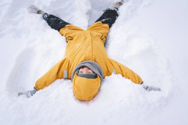 Parlak sarı ceketli neşeli bir çocuk kış boyunca taze karda oynuyor.