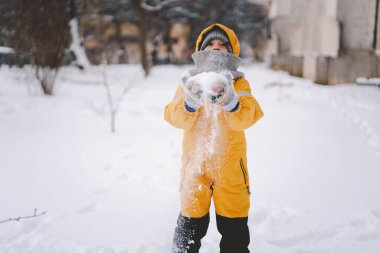 Parlak sarı ceketli neşeli bir çocuk kış boyunca taze karda oynuyor.