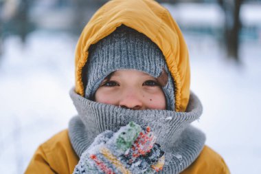 Neşeli bir çocuk kış havasının keyfini çıkarır, sıcak giysiler içinde parlak sarı bir ceket ve karla çevrili samimi bir şapka da dahil..