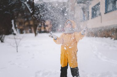 Parlak sarı ceketli neşeli bir çocuk kış boyunca taze karda oynuyor.