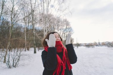 Kırmızı eşarplı gülümseyen bir kadın, parlak mavi gökyüzünün altındaki sakin bir ormanda karlı bir kış gününün tadını çıkarıyor. Noel ve Yeni Yıl Kutlama Konsepti.