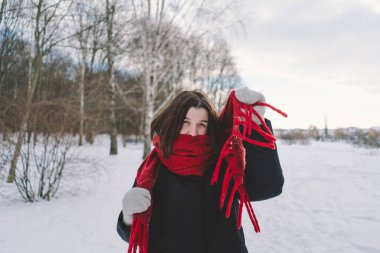Kırmızı eşarplı gülümseyen bir kadın, parlak mavi gökyüzünün altındaki sakin bir ormanda karlı bir kış gününün tadını çıkarıyor. Noel ve Yeni Yıl Kutlama Konsepti.