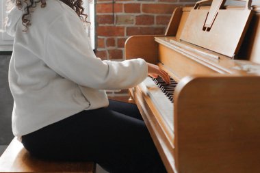 Kıvırcık saçlı bir kadın piyanonun başında oturmuş, güzel ışıklandırılmış oturma odasında yarattığı müziğin keyfini çıkarıyor..