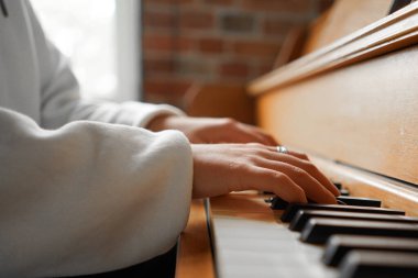 Kıvırcık saçlı bir kadın piyanonun başında oturmuş, güzel ışıklandırılmış oturma odasında yarattığı müziğin keyfini çıkarıyor..